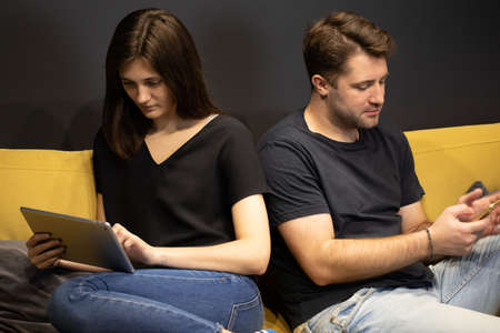 Attractive Couple using smartphone and tablet chatting online ignoring anotherの写真素材