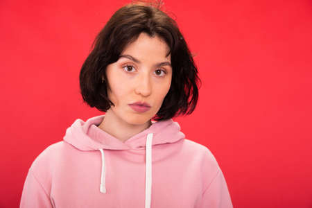 Close-up young sexy brunette woman looks at camera on red background. Copy spaseの写真素材