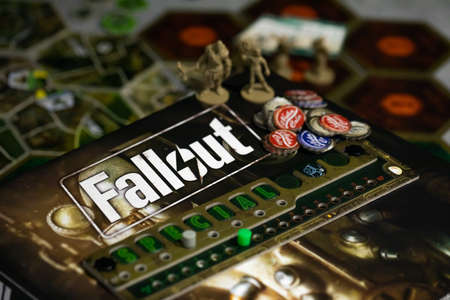 Roseville, MN, USA, 02.04.2021 - Fallout strategy post-apocalyptic Board Game components on Map Tiles close up. Caps Tokens Nuka Cola and Player Board on cardboard box with Fallout logo.のeditorial素材