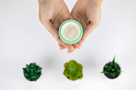 Close-up hands hold cosmetic jar with cream on white background with plantsの写真素材