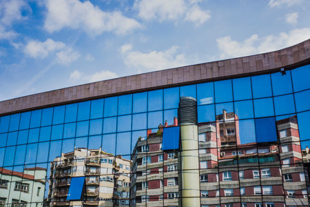 Girona, Spain, May 1, 2020 - Gironas residential blocks are reflected in glass of modern building. Concept of old and new architecture, copy space on blue sky. diagonal line between sky and cityのeditorial素材