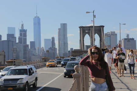 New York City, NY, USA 2.09.2020 - Pretty long hair brunette girl posing on Brooklyn Bridge in front of tourist group and car traffic. Brooklyn Bridge in NY is one of most visited places in U.S.のeditorial素材