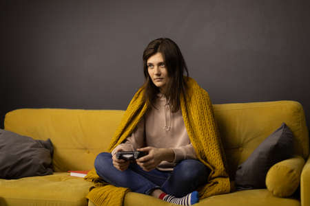 Attractive long-haired girl Playing Videogame alone sitting on comfy yellow sofaの写真素材