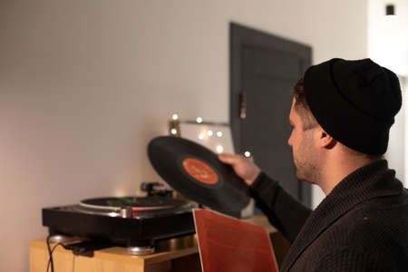 Young unshaven handsome hipster guy puts record on turntable from red envelope