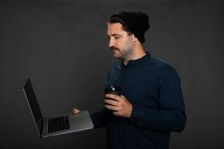 Stylish freelancer male remote employee looking at laptop screen holding coffee