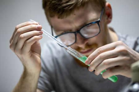 bearded biologist in glasses conducts chemical experiment with green reagentの写真素材