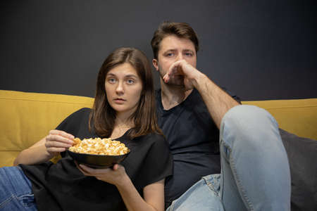 Couple watching tv movie hugging lying on couch eating popcorn at homeの写真素材