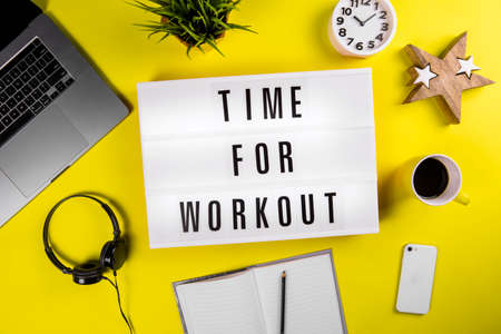 Lightbox with text TIME FOR WORKOUT on yellow background with laptop, smartphone, headphones and notes. Concept of change of scenery of office workspace, keep-fit, physical exercise session, trainingの写真素材