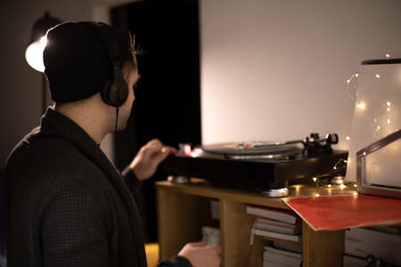 Young unshaven handsome hipster guy push start button on turntable backlitの写真素材