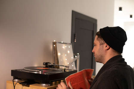 Young unshaven handsome hipster guy puts record on turntable from red envelopeの写真素材