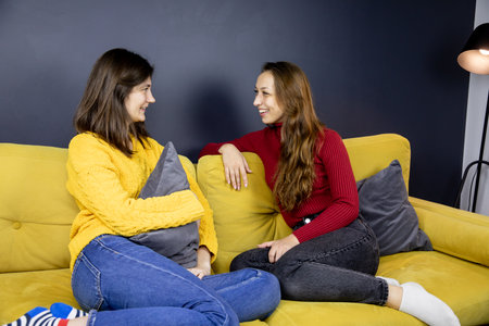 young lesbian couple sit on comfy sofa knees bent Talking cheerfully laughingの写真素材