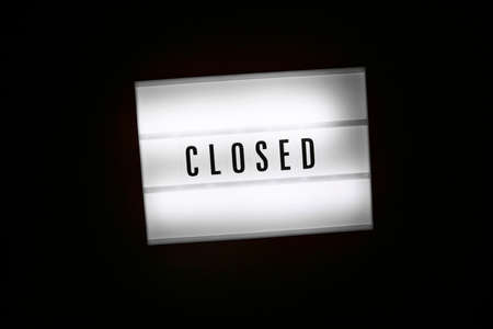 Lightbox with text message CLOSED isolated on black background. Inscription glows in dark. Not opened shops, business, restaurant, door closed, economy society borders closed due to lockdown conceptの写真素材