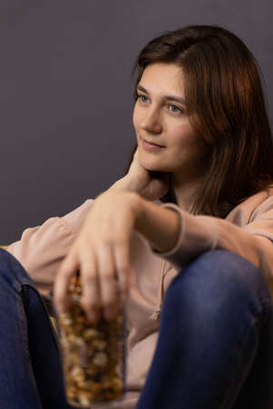long-haired brunette girl sitting knees bent hold plastic cup of popcornの写真素材