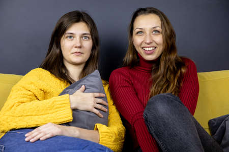 young lesbian couple sit on comfy sofa knees bent huddled together watching TVの写真素材