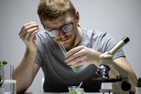 bearded biologist in glasses conducts chemical experiment with green reagentの写真素材