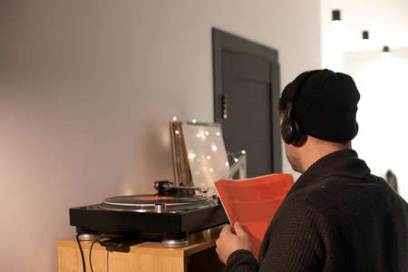 Young unshaven handsome hipster guy puts record on turntable from red envelopeの写真素材