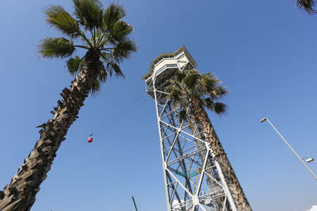 Barcelona, Spain, March 1, 2020 - Bottom-up view of Montjuic cable car tower and palm tree on cloudless blue sky backdrope. Competition between natural and man-made skyscrapersのeditorial素材