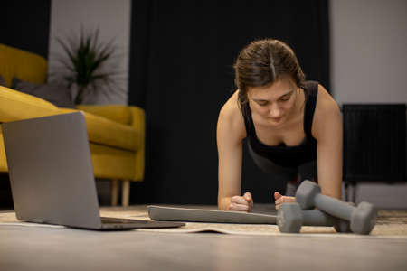 Young woman enjoys bodybuilding training abs exercise, stands in plank indoorの写真素材