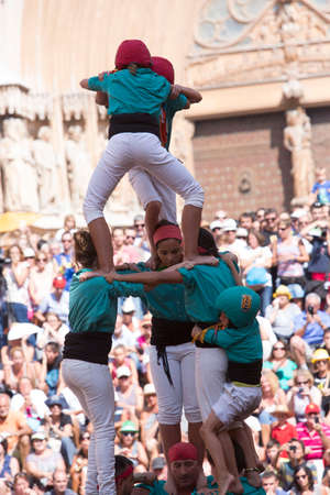 Tarragona, Spain, September 19, 2019 - Children complete erection of human castells tower by climbing to top. Dangerous tense moment close-up. Risk of falling from height conceptのeditorial素材