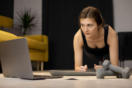 Young woman enjoys bodybuilding training abs exercise, stands in plank indoorの写真素材