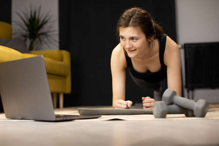 Young woman enjoys bodybuilding training abs exercise, stands in plank indoorの写真素材