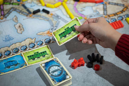 London, GB 11.02.2021 - Popular family railway-themed board game Ticket to Ride Europe edition. Player pick up train cards , map with colorful train cars and station out of focusのeditorial素材