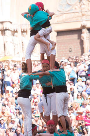Tarragona, Spain, September 19, 2019 - Children complete erection of human castells tower by climbing to top. Dangerous tense moment close-up. Risk of falling from height conceptのeditorial素材