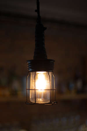 Stylish retro electric light in protective metal grid on blurred brown background. Loft style in interior, industrial lighting designの写真素材