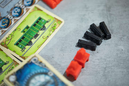 London, GB 11.02.2021 - Close-up view of popular family railway-themed board game - Ticket to Ride Europe edition. Gameplay elements: black plastic train cars, red stations and train cards near mapのeditorial素材