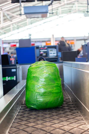 backpack is wrapped in green plastic wrap weighed at check-in counter before departure at Prague Airport. concept of safe travel, luggage security. Plastic pollutionの写真素材