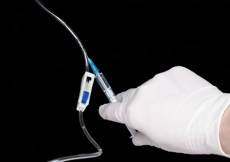 Hand in medical gloves, disposable infusion set. Black background