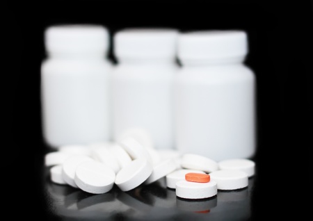 White medicine bottle, color pills on black background.
