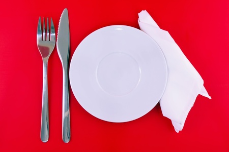Table serving-knife,plate,fork and silk napkin  on  red colour background.の写真素材
