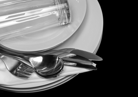 Pile of white plates, glasses with forks and spoons on silk napkin. Black backgroundの写真素材