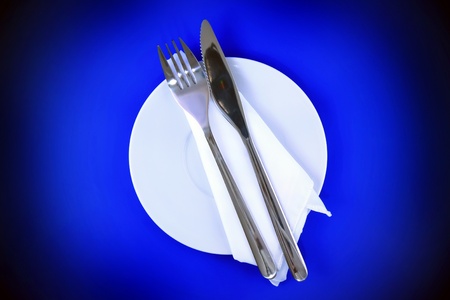 Table serving-knife,plate,fork and silk napkin  on  blue colour background.