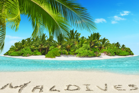 Whole tropical island within atoll in tropical Ocean. Uninhabited and wild subtropical isle with palm trees. Inscription "Maldives" in the sand on a tropical island,  Maldives.の写真素材