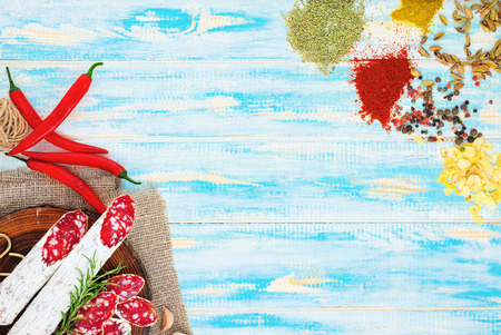 Sliced cured sausage with spices and a sprig of rosemary on blue wooden rustic background.の写真素材