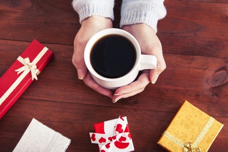 coffee in hands with gifts on a wooden backgroundの写真素材