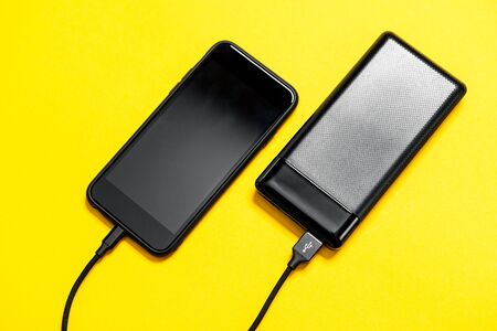 Black Power bank charges smartphone isolated on yellow background