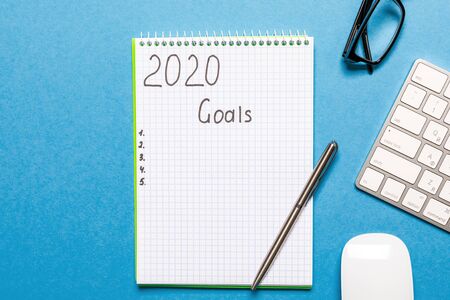 2020 GOALS on his notebook. New year resolutions concept. Top view. isolated on blue background