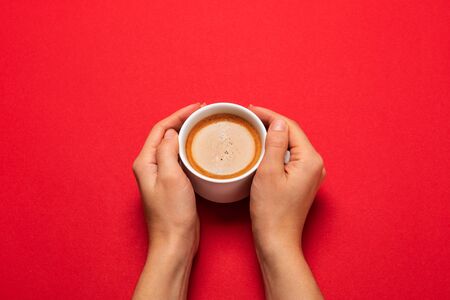 Female hand holding a white cup with black coffee on a red background.の写真素材
