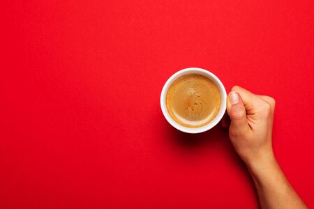 Female hand holding a white cup with black coffee on a red background.の写真素材