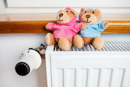 Two teddy bears are sitting on a radiator in the houseの写真素材