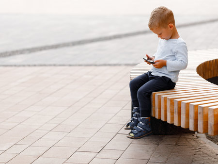 boy playing on the phone while sitting on a benchの写真素材