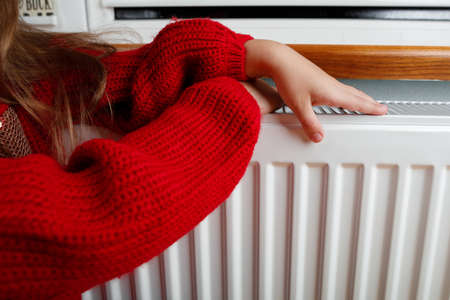 a little girl warms her hands and feet on a radiator