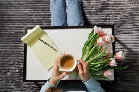 girl sitting on the couch with a cup of coffee and a notebook in her hands. Love, valentines day concept.の写真素材