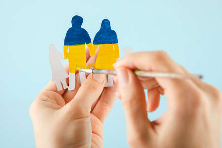 Woman hands hold a paper-cut family painted in the national colors of Ukraine. Ukrainian flagの写真素材