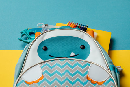 Backpack with school supplies on a blue and yellow background. View from above. copy space. Back to...