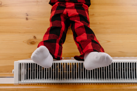 Girl warm ones hands near radiator at home.の写真素材