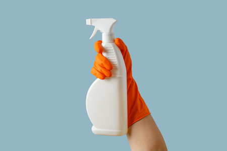 hand with orange rubber glove holding cleaning supplies isolated on blue background. bannerの写真素材